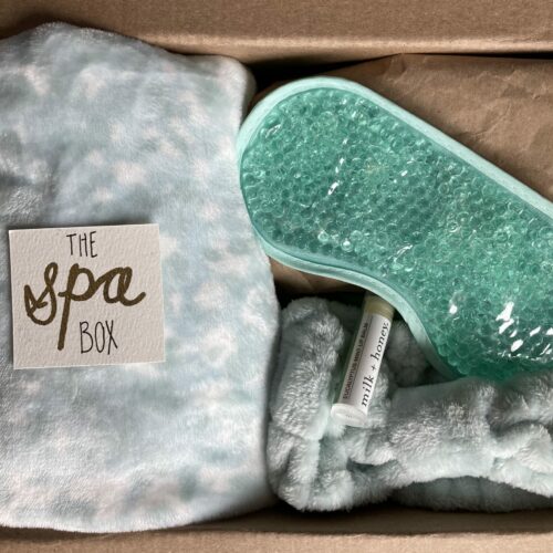 Care package with spa theme including cozy blanket, eye mask, hair band and spa tools all in blue-green tones